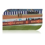 Manchester United advertising banner displayed at a stadium with security personnel in the background.